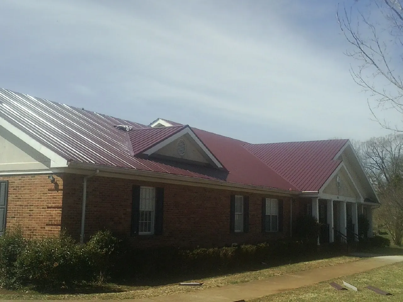 Red metal roof with gabled entries on a long brick building, from a Hail Damage Roof Repair job in Ledgewood