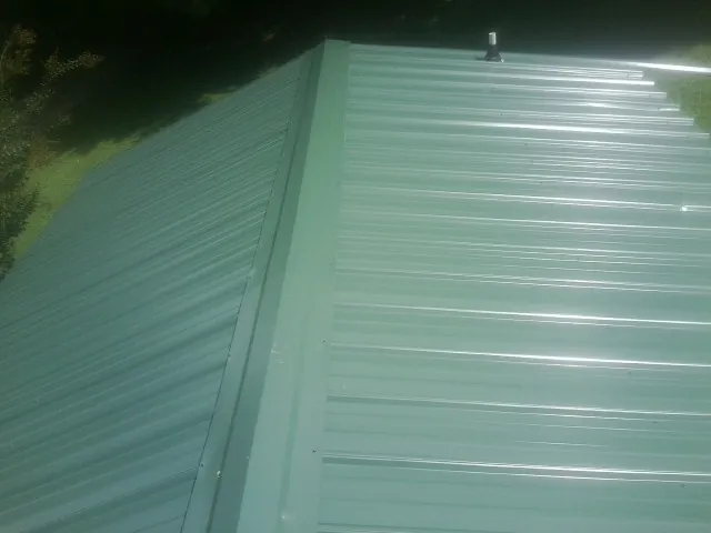 New green metal panels meeting at the ridge of a roof — Flat Roof Repair work by our crew in Ledgewood