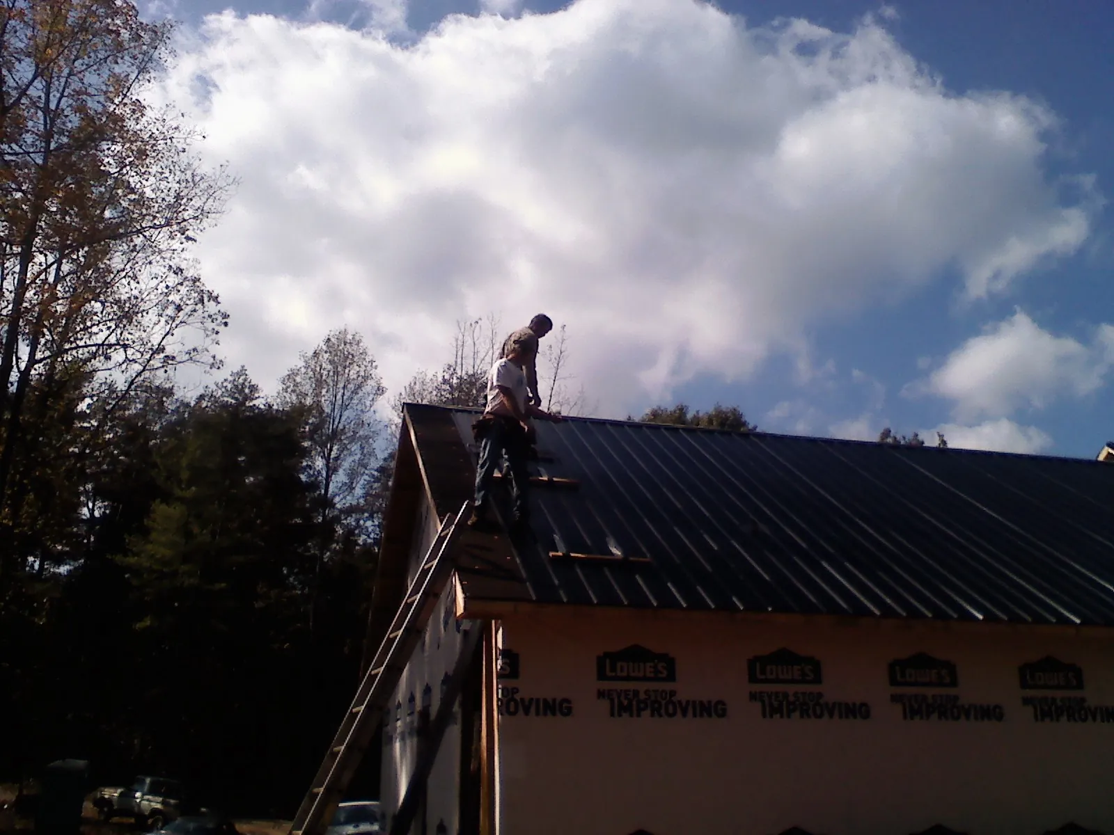 Roofer fastening dark metal panels high against a cloudy sky, from a Roof Inspection job in Ledgewood