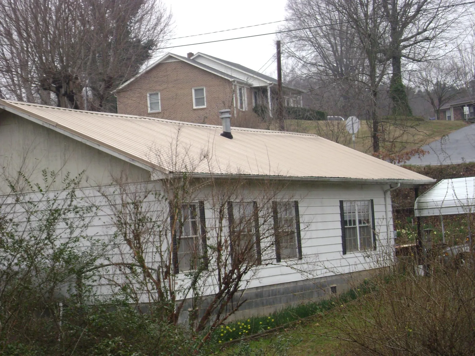 Tan metal roof on a white sided house set into a hillside — Commercial Roofing by Roofing Brothers in Ledgewood